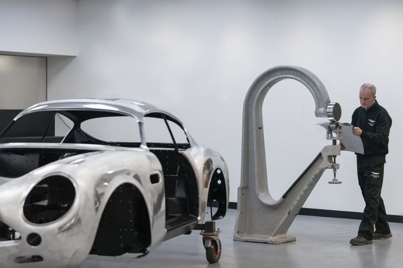 Man shaping metal on an English Wheel with DB4 GT Zagato Continuation in foreground. 